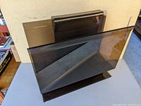 Front and side view of the dark tinted acrylic magazine stand showing its shape and material.