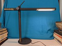 Front-side view of the modernist adjustable desk lamp showing the cylindrical horizontal light arm, lever adjustment, and heavy round metal base.