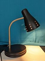Photo of the black desk lamp with perforated shade lit up demonstrating the touch light control feature.