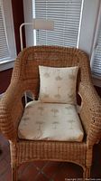 Front view of wicker arm chair with beige cushions featuring palm tree print and metal floor lamp behind it