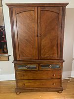 Front view of closed armoire showing double doors, slate-detail upper drawers and bun feet