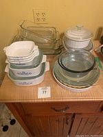 Full view of Corningware bowls, clear glass baking dishes, and white ceramic casserole on wooden counter.