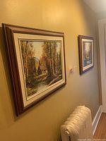 Two framed oil paintings of cabin scenes by C H Bajeaux displayed on a wall.
