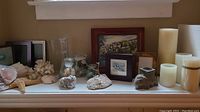 Wide shot of all items grouped on a white ledge, showing candles, shells, coral, starfish, picture frames and framed print