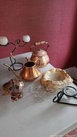 Photo showing copper teapot, watering can, marble ashtray, candle holders, and wire bicycles on a white surface