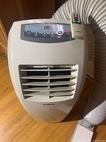 Front view of GoldStar portable air conditioner with digital control panel and remote on top, vent hose connected to side.