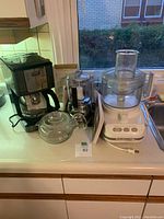 Lot items on kitchen counter: KitchenAid food processor on right, Cuisinart chop and grind on left, kitchen torch box behind them, and black coffee pot next to them.
