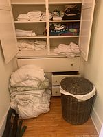 Photo of linen closet with folded towels, linens, and wicker laundry basket on the floor and in shelves.