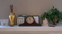 Wide view of mantle displaying the clock, framed print, ceramic vase, and decorative items