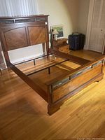 Full view of queen size wooden bed frame assembled without mattress, showing headboard, side rails, and footboard in a bedroom.