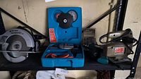 Black and Decker SawForce circular saw on left, blue clamshell case with drill and accessories center, Black and Decker jigsaw right on shelf