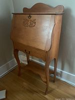 Front angle view of the wood secretary desk showing the carved appliqué on the drop front door and the lower drawer with handles.