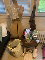 Full view of Acme dress form with sequin fabric draped over left shoulder, small wooden table with sewing patterns and thread spools.