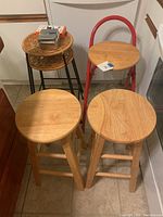 Four stools grouped showing two wooden stools, one wood and steel stool with red frame, and one metal and wicker stool.