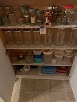 Full shelf view showing multiple sizes of glass canning jars with various lids, large glass storage jars, and stacked plastic Tupperware containers with lids.