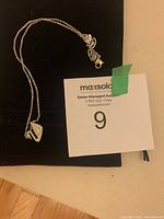Silver-tone Swarovski necklace with swan pendant laid flat on black pouch with auction tag nearby.