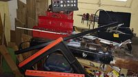 View showing red metal tool boxes on workbench with assorted hand tools on top, bench grinder visible, plastic sawhorses leaning against bench, and wood cutoffs behind.
