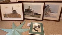 Overall view of three framed prints featuring historical buildings and a painted blue 7-pointed tin star placed in front.