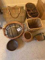 Photo showing eight wicker and woven baskets of various shapes and sizes including a rectangular picnic style basket with handles, oval baskets, square basket, round basket with beads, and small green decorative basket.