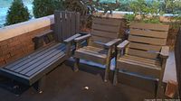 Photo showing entire set of outdoor wood furniture on patio including one chaise lounge and two chairs with weathered gray paint and peeling.