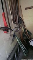 Wide angle showing tools leaning against garage wall including ladder base and string trimmer hanging