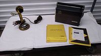 Overview of the antique brass candlestick phone, Heathkit radio, and manuals laid on a white cloth against a storage background.