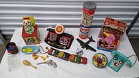 Wide shot showing a variety of vintage toys including a clown jack-in-the-box, tin Junior Dial Typewriter, Tinkertoys container, bubble blowing elephant, toy airplane, toy phone, Barrel of Monkeys game, and miscellaneous small toys.