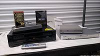 Full view of all media players, VHS rewinder, DVDs, and tapes together on table from front angle.