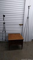 Photo showing wooden end table and two camera tripods against a storage unit door backdrop.
