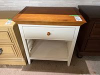 Front view of the two-tone American Drew wood bedside table showing drawer, lower shelf, and slatted side panels.