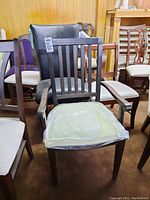 Front angled view of dark wood framed armchair with vertical back slats and upholstered seat covered partly with protective plastic.