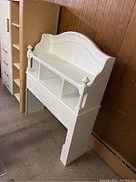 Front view of the white wooden bookshelf headboard showing the top shelf, cubby compartments, and decorative elements.
