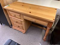 Front side view of Broyhill wooden desk showing three drawers on left and one centered drawer with wooden knobs and turned legs.