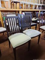 Pair of dark wood chairs with vertical back slats and light upholstered seats. Shows minor scratches and typical floor model wear.
