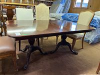 Full view of the wood dining table showing the polished tabletop and claw foot pedestal bases, surrounded by chairs.