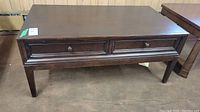 Full view of the dark wood coffee table showing front with two closed drawers and straight legs.