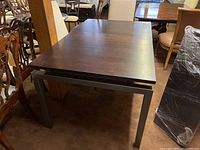Dining table narrow without leaves attached showing dark wood top and rectangular metal legs in dark gray finish