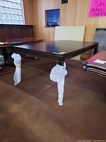 Photo of the wood dining table showing the rectangular top with a dark wood finish and protective wrapping on the legs.