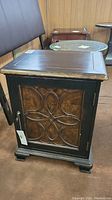 Front view of the dark wood side table with carved door panel showing decorative pattern and key lock.