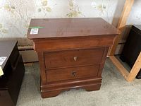 Front view of Kincaid wood bedside table showing three drawers with keyholes, metal pulls, and curved base design.