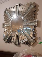 Front view of sunburst style wall mirror showing central round mirror and radiating rectangular mirrored panels with decorative bead accents.