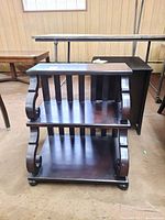 Front view of dark wooden side table with two open shelves and decorative curved sides.