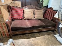 Front view of three seat sofa with brown leather back, velvet seat cushions, and four throw cushions including striped and solid designs.