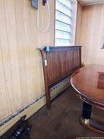 Solid oak king size headboard standing upright against a wall in a room with wood paneling and a window above.