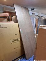 Solid oak table top leaning against boxes in storage environment, showing full length and wood grain texture.