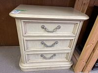 Front view showing three metal pull drawers and rounded edges on cream finish bedside table.