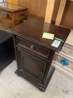 Front view of Stanley Furniture bedside table showing drawer and closed lower cabinet door with metal pulls, dark wood finish, and decorative molding at base.