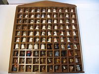 Full view of wooden rack filled with 100 thimbles under plexiglass