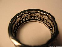 Close-up photo of the ring's inner band showing 'ONE DOLLAR' engraving and design details.