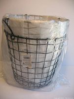 Photo of one black round metal wire basket with a white fabric liner inside and original packaging plastic wrap around.